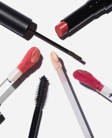 Overhead flat lay of beauty products including lip gloss wands, lipstick, and mascara brushes on a white background