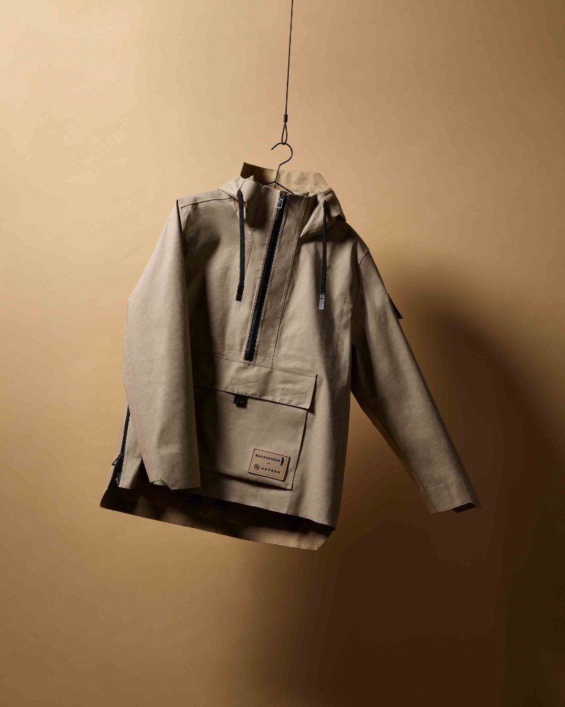 Tan hooded jacket with a quarter-zip, hanging on a wire hanger against a neutral background in a studio-style setting. Apparel photography.