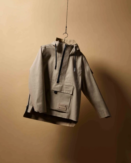 Tan hooded jacket with a quarter-zip, hanging on a wire hanger against a neutral background in a studio-style setting. Apparel photography.