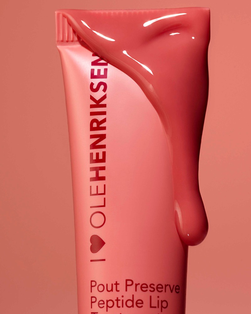 Close-up of a pink Ole Henriksen Pout Preserve Peptide Lip Treatment tube with lip treatment dripping down the side on a pink background.