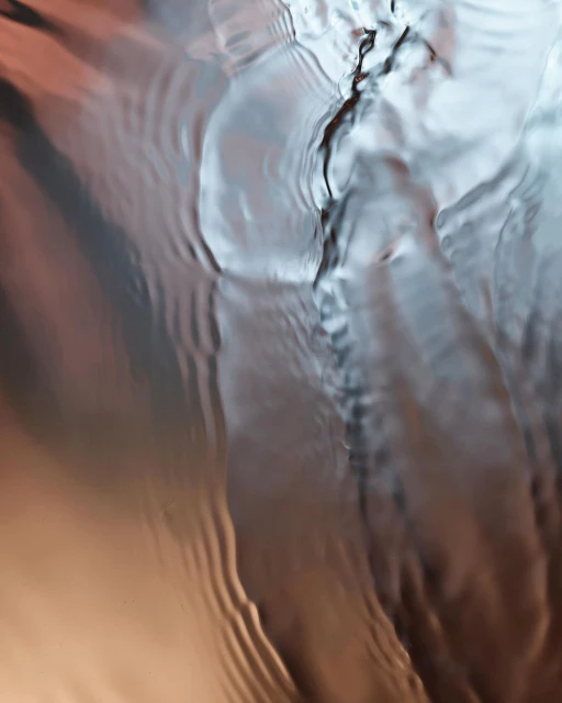 Abstract water surface with rippled texture, reflecting light in shades of grey, silver, and copper.