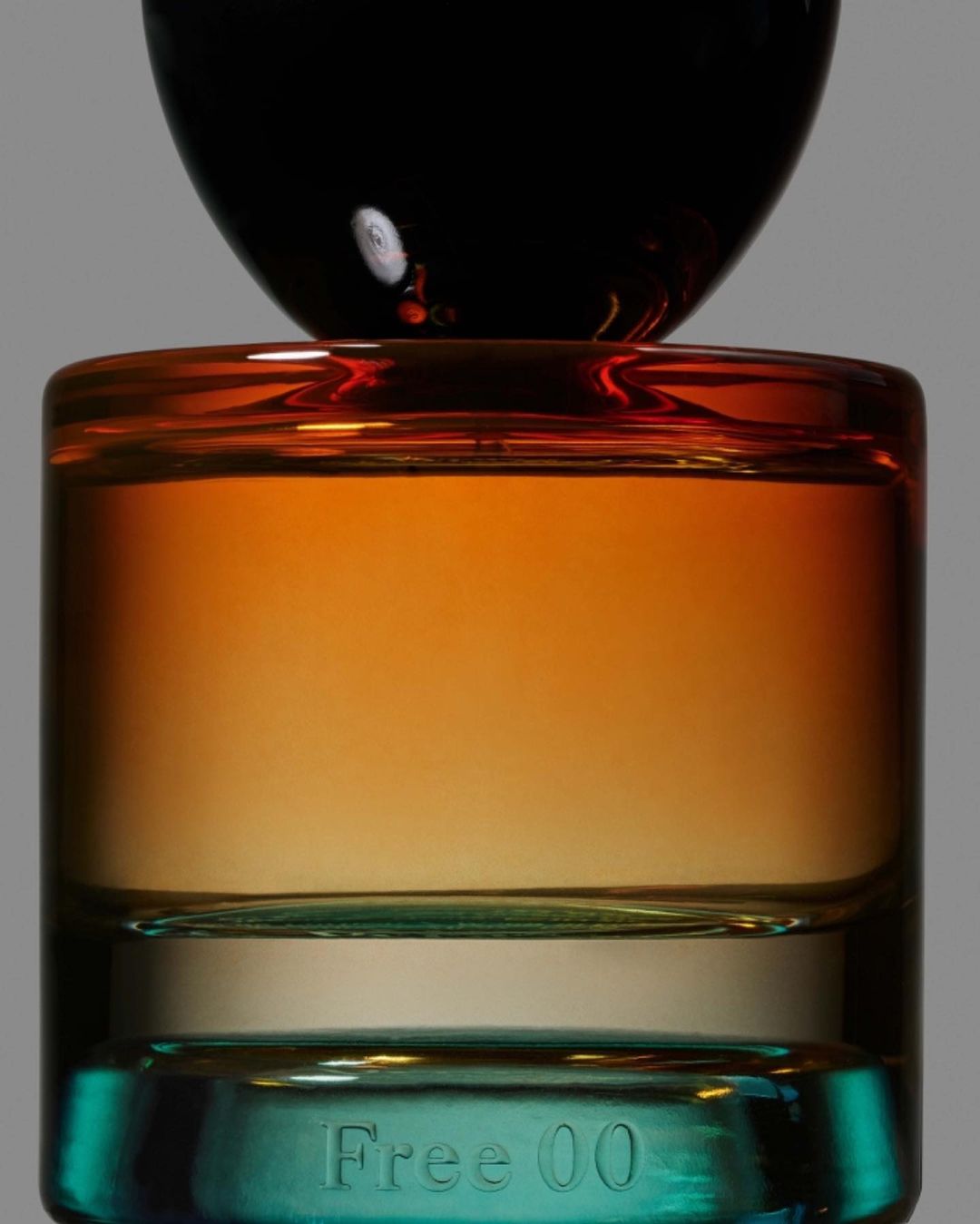 Close-up studio shot of a multi-colored glass perfume bottle, featuring amber liquid inside and text 'Free 00' at the base.