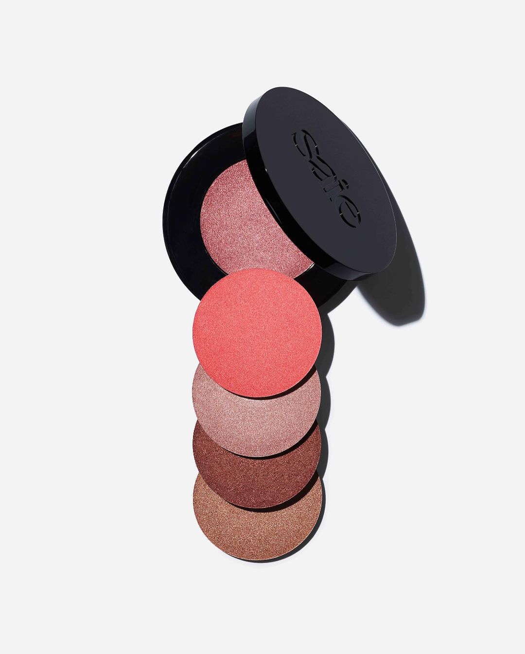 Elevated, close-up studio shot of opened makeup compact with black case and tiered circular blush refills on a bright white background.