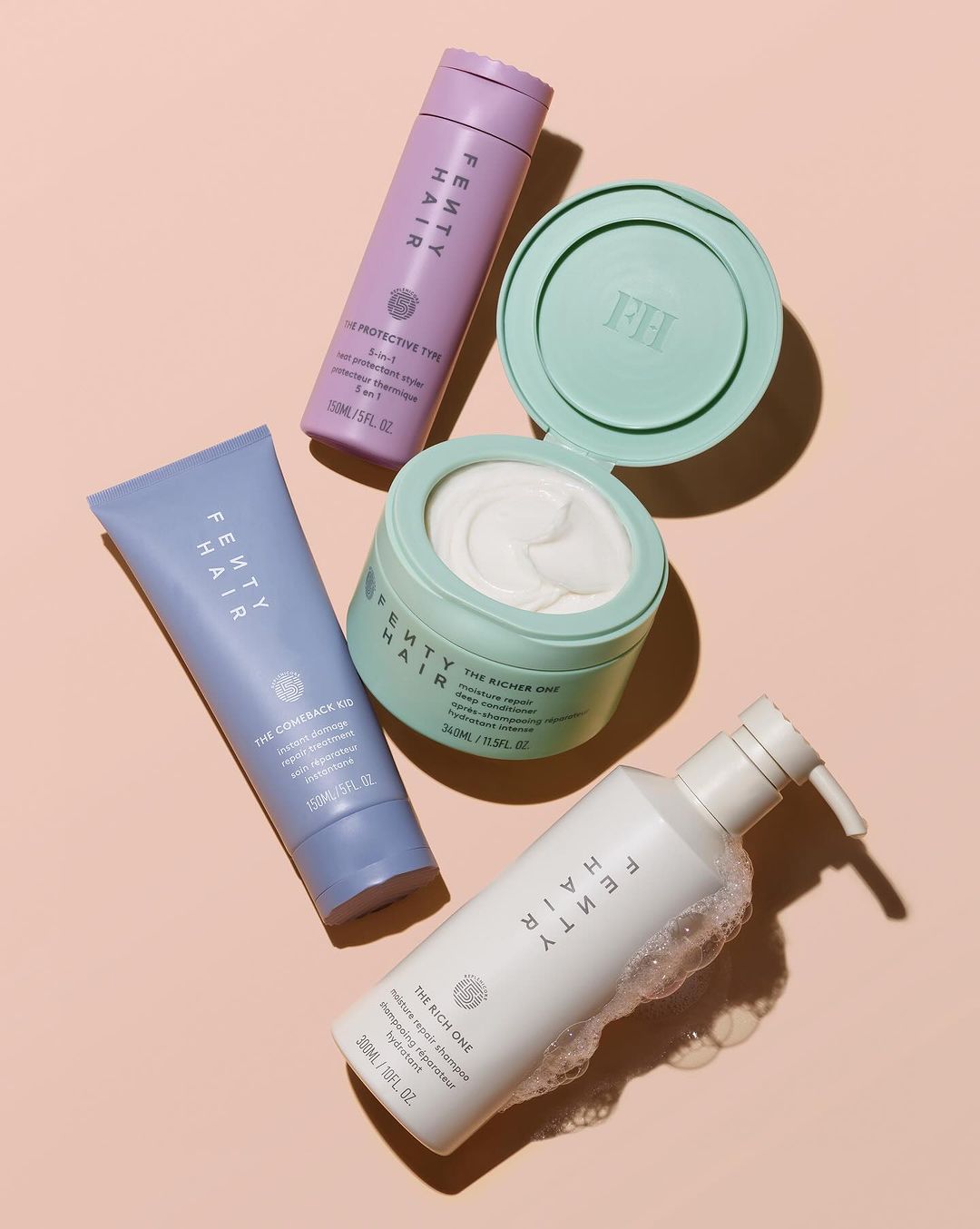 Fenty Hair products flat lay. Includes shampoo, conditioner, hair mask, and heat protectant spray. Pale pink backdrop. Beauty product photography.