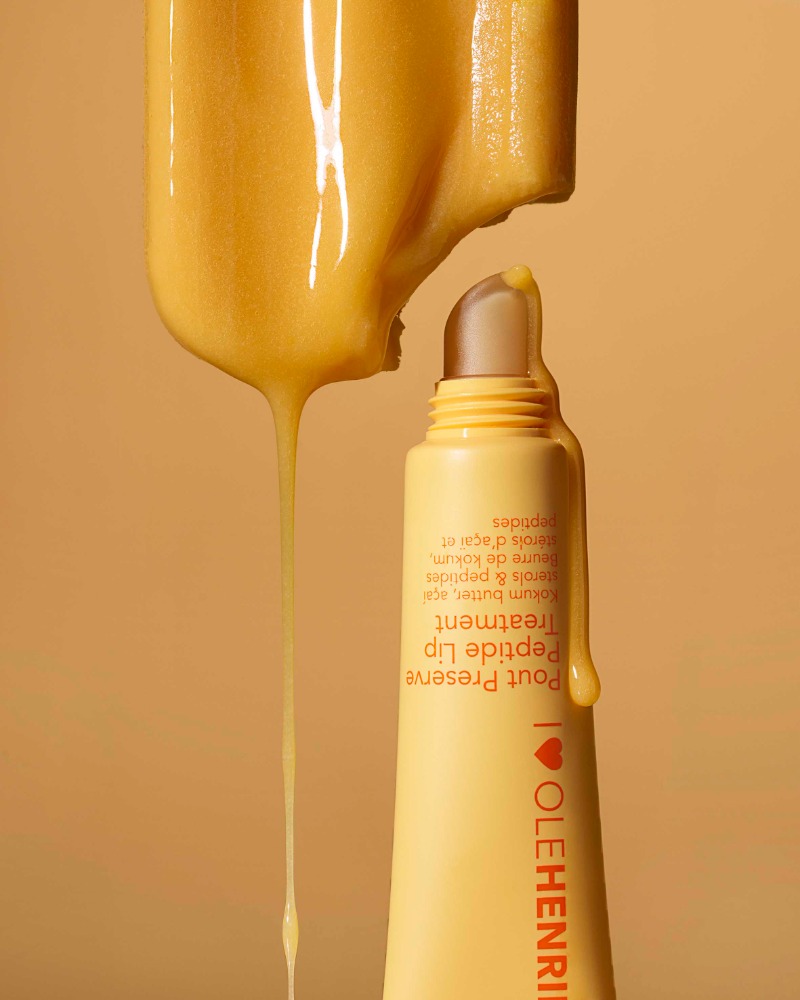 Close-up of yellow lip treatment product with dripping serum. Cosmetic product shot with simple background for beauty advertising.