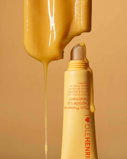 Close-up of yellow lip treatment product with dripping serum. Cosmetic product shot with simple background for beauty advertising.