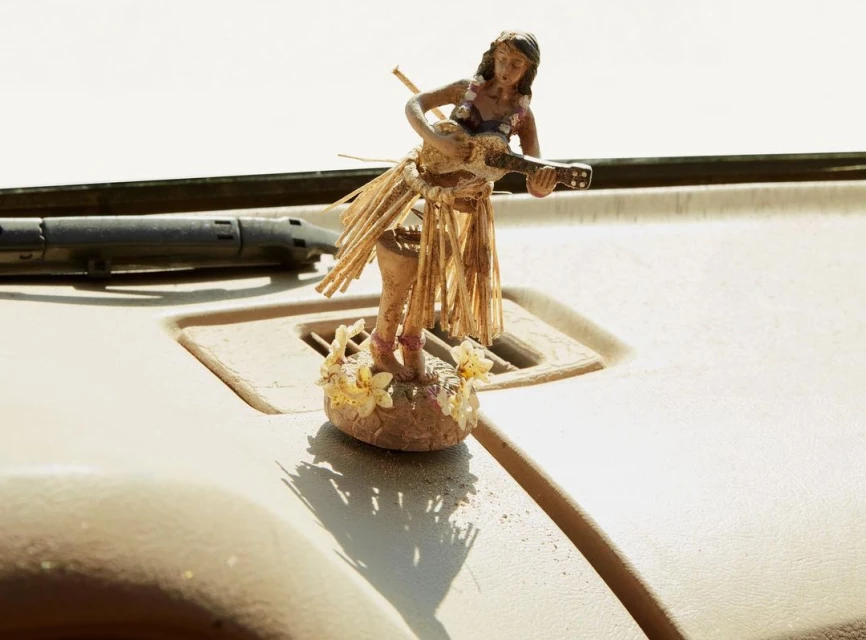 Hawaii hula doll playing a ukulele, wearing a grass skirt and flowers on a car dashboard, sunny lighting, vacation vibes.