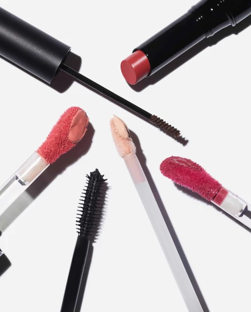 High-angle product shot of assorted makeup: lipstick, mascara wands, and lip gloss applicators arranged on a white surface.