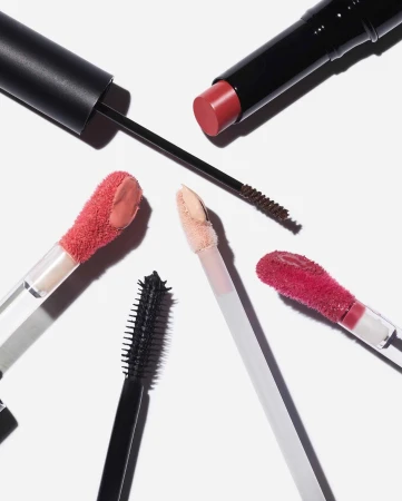 High-angle product shot of assorted makeup: lipstick, mascara wands, and lip gloss applicators arranged on a white surface.