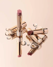 Close-up product photography of rose-toned lipsticks with glossy water droplets on a reflective metallic surface.