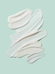 White cosmetic cream smeared across a light green background, showing smooth texture and ridges.