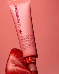 Pink lip treatment tube resting against a sliced strawberry with dripping juice against a matching pink background