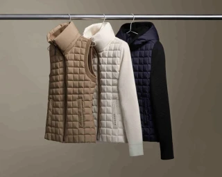 Three quilted outerwear garments hanging on silver hangers from a metal rod against a plain neutral background.