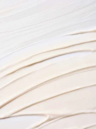 Close-up macro shot of smooth cream texture swatches on a plain white background by Dimitri Newman.