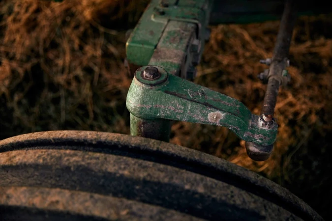 Close-up of the front wheel, axle, and suspension components of a vintage green tractor in a rural setting with dry grass.