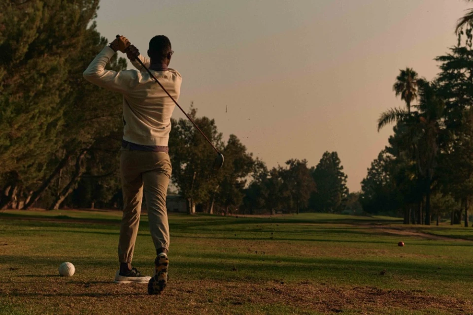 An adult male golfer in mid-swing on a green golf course with trees and a light sky during daytime, showcasing athletic outdoor activity.