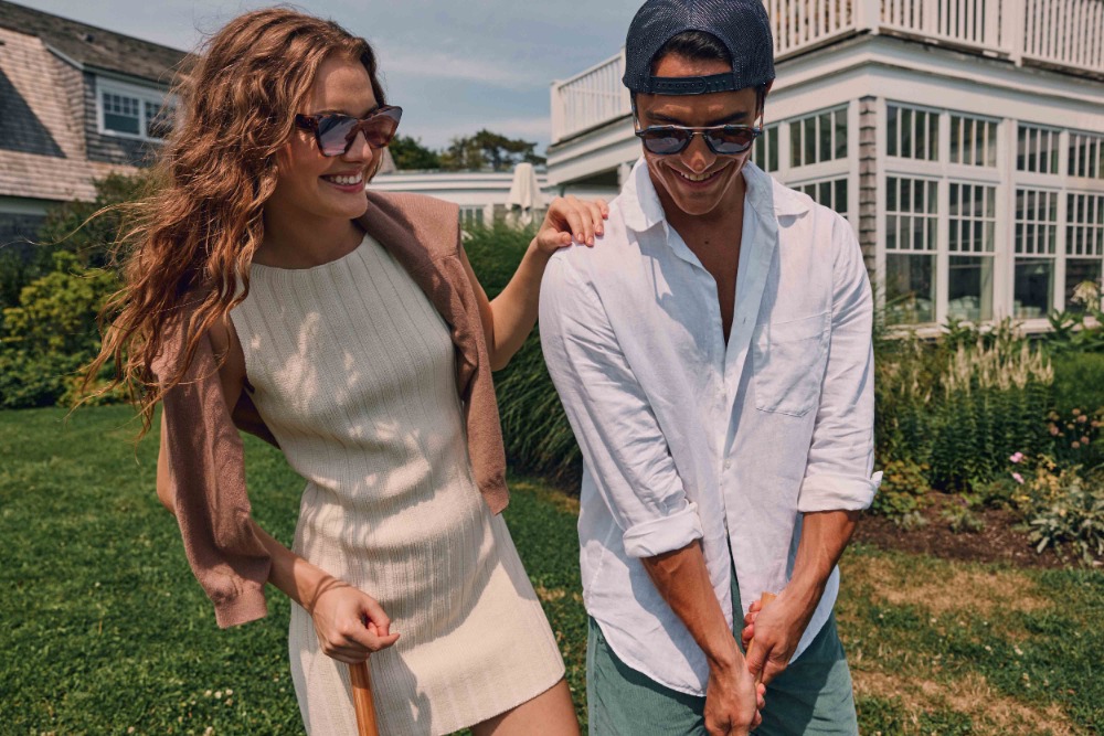 Man and woman smiling outdoors, wearing sunglasses and casual summer apparel, photographed by John Schell.