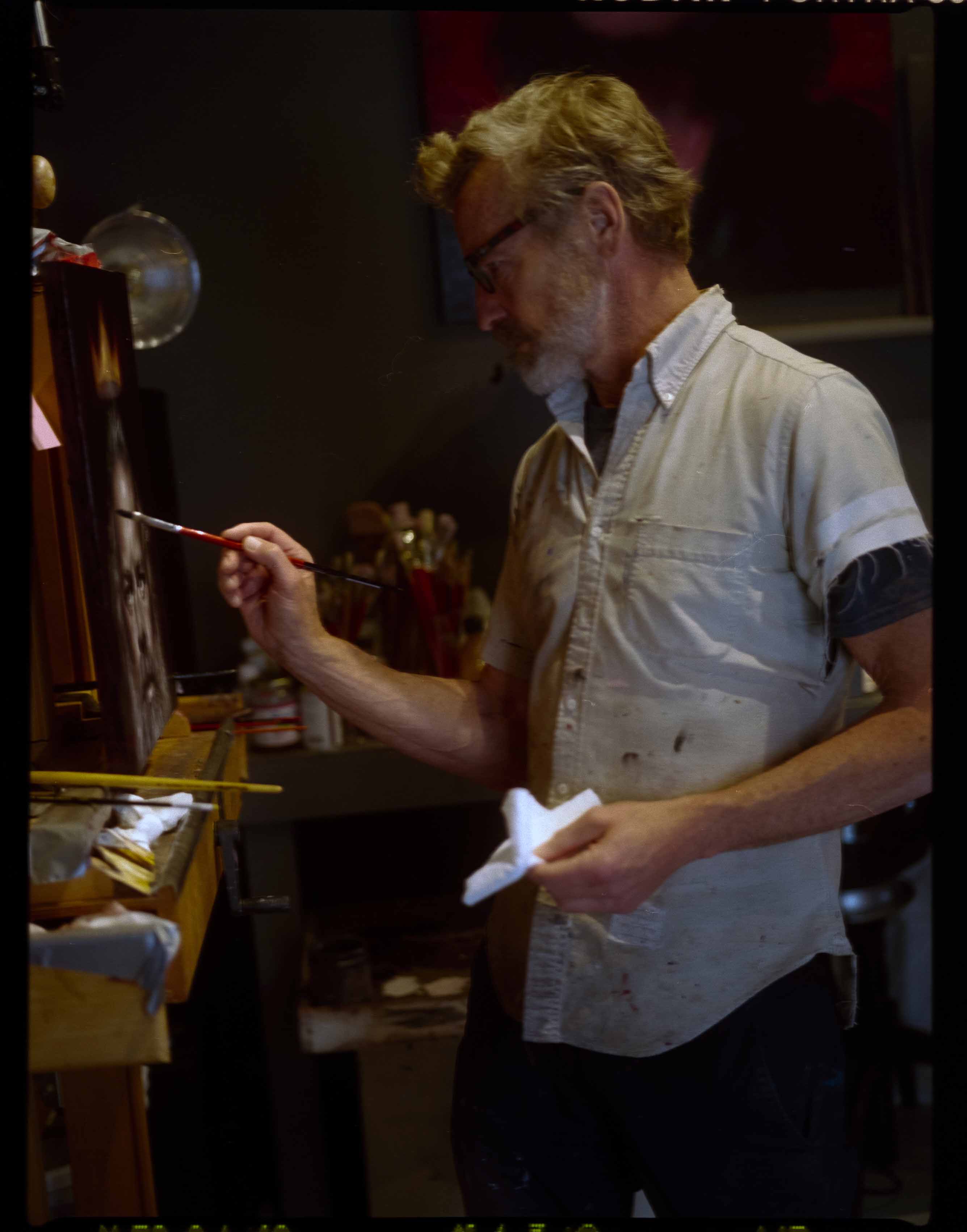 Artist painting on canvas in a studio, holding a paintbrush in one hand and a cloth in the other, capturing a creative moment.