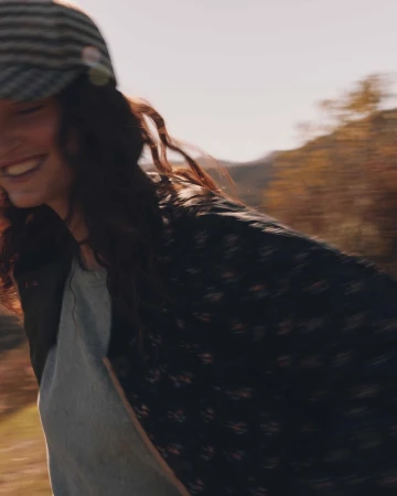 Smiling woman in a patterned cap and dark patterned jacket outdoors with motion blur captured by John Schell