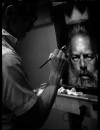Monochrome portrait of an artist in profile painting a detailed self-portrait on canvas in a dark studio.