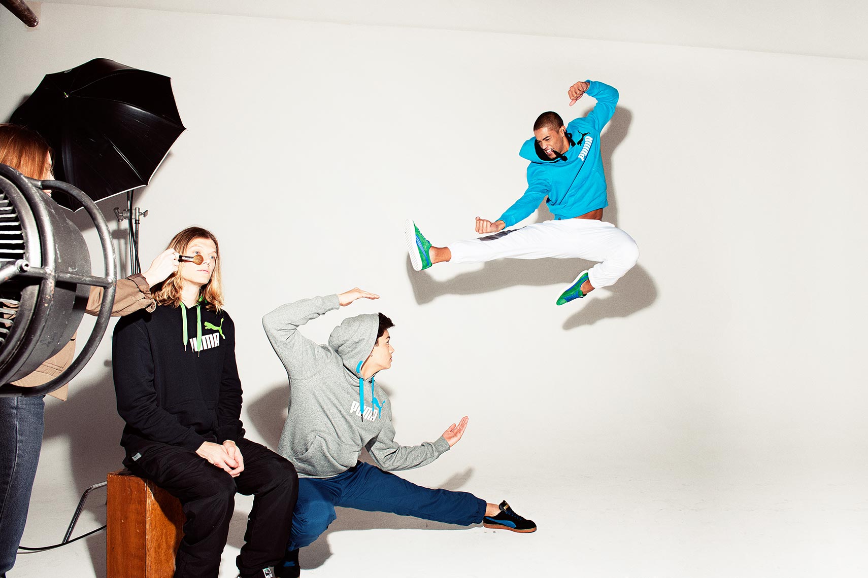 Action shot of three people in a photo studio wearing Puma branded athletic clothing, one jumping in the air in a karate style pose.