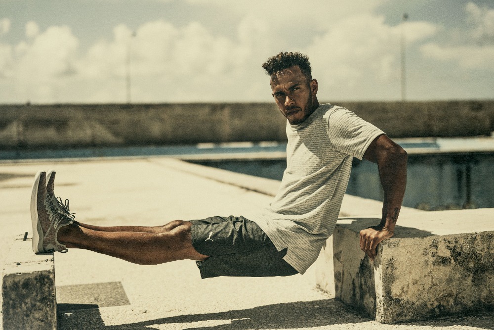 Adult man in athletic wear outdoors performing tricep dips on concrete blocks against a cloudy sky, looking at the camera.