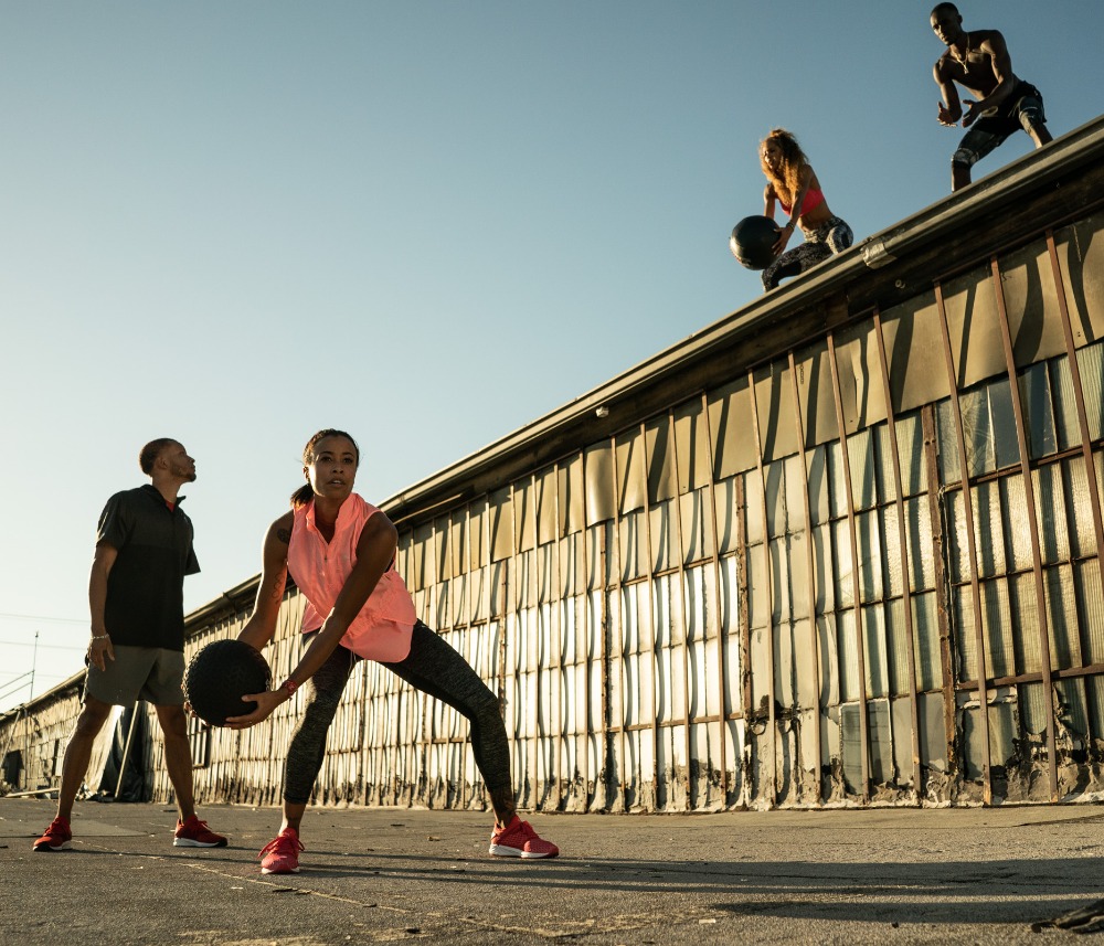 Group of athletic people exercising outdoors with medicine balls on a sunny day, wearing activewear and athletic shoes, training together.