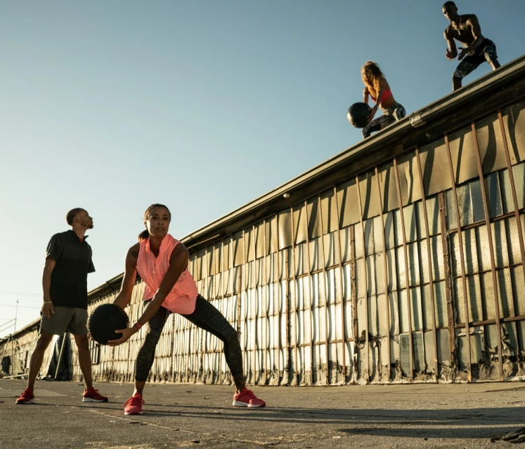 Group of athletic people exercising outdoors with medicine balls on a sunny day, wearing activewear and athletic shoes, training together.