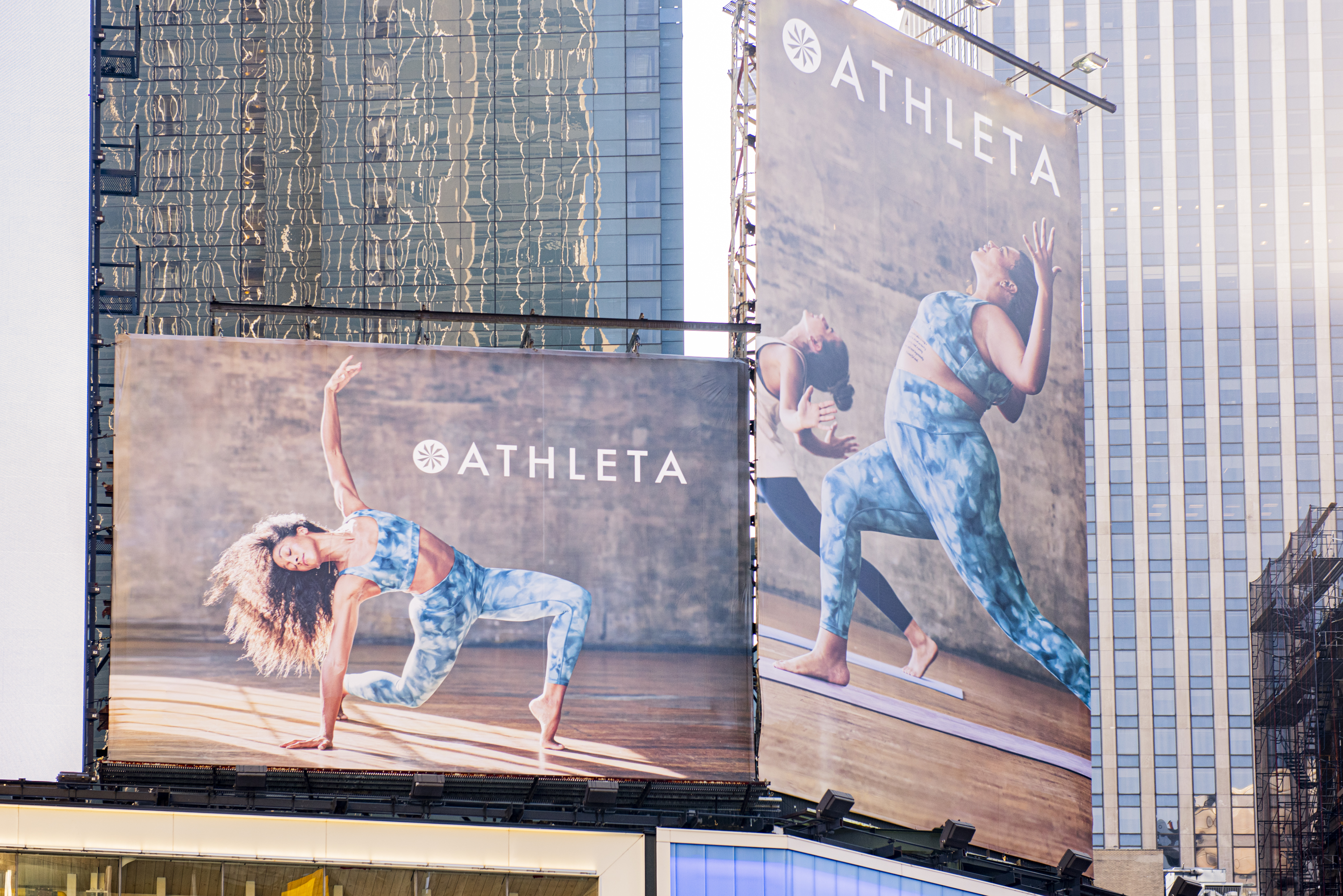 Two large Athleta billboards in an urban setting feature athletic women in tie-dye outfits, set against a backdrop of modern buildings.