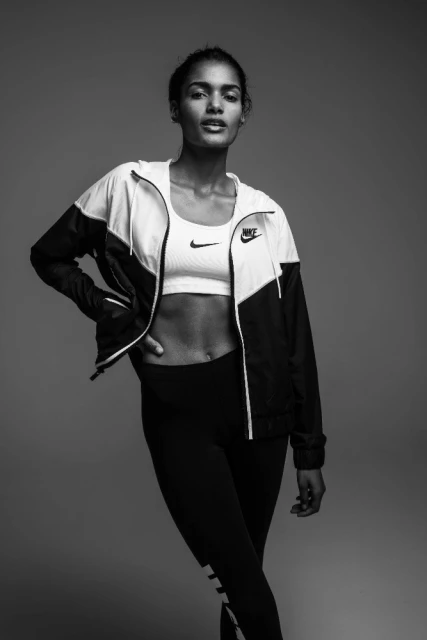 Athletic woman in sports bra and jacket poses confidently in a studio setting showcasing fitness apparel and a healthy lifestyle.