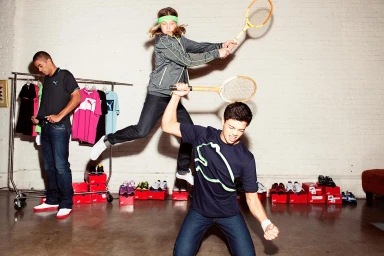 Three young men posing dynamically indoors with vintage tennis rackets and athletic apparel by photographer Jon Johnson.