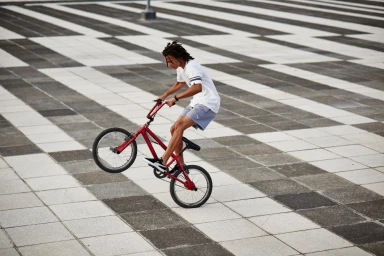 Young Black man riding a red BMX bike on a paved public square with a black and white checkerboard pattern