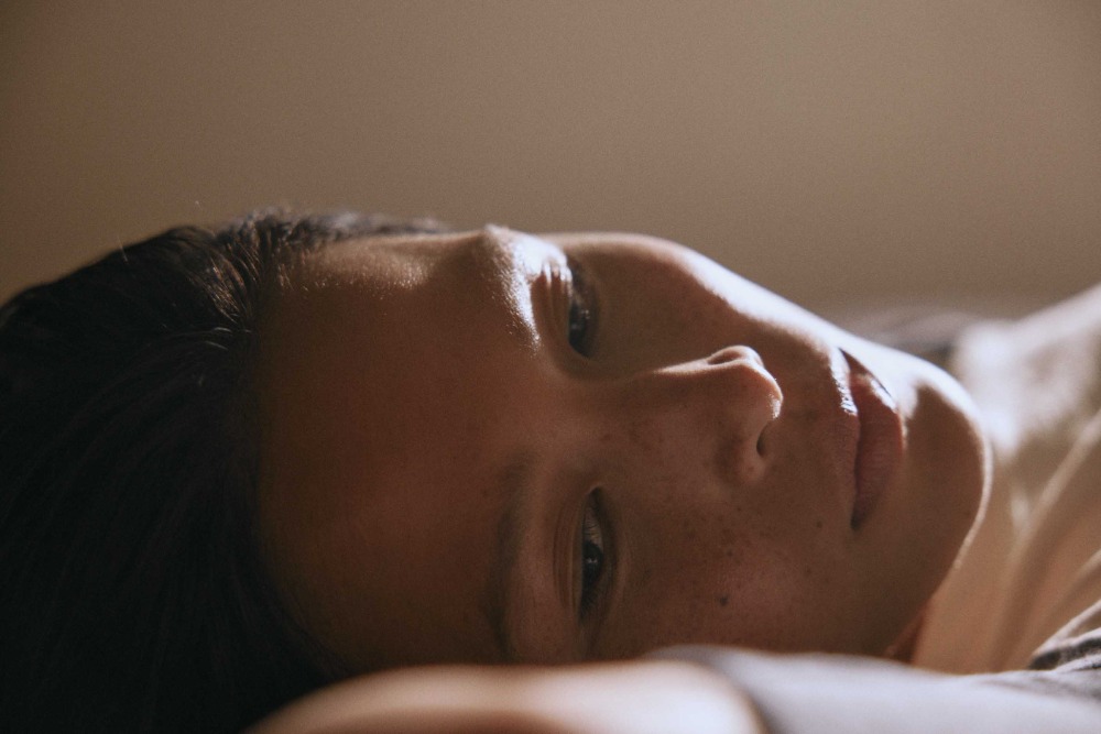 Close-up portrait of an adult female lying down, with soft, diffused lighting illuminating her face, creating a warm and intimate mood.