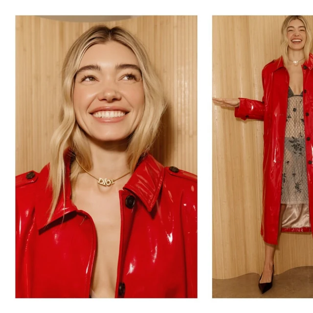Blonde woman in a red coat with a choker necklace smiles against a light wooden wall with vertical stripes. Fashion editorial shot.