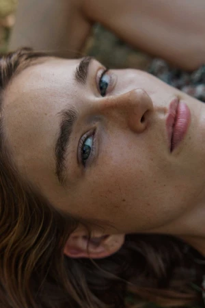 Close up portrait of a young woman with freckles and brown hair looking directly at the camera outdoors