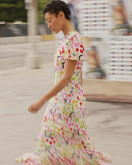 Woman in a vibrant, patterned midi dress walks on a concrete street with motion blur, showcasing a fashion editorial style.