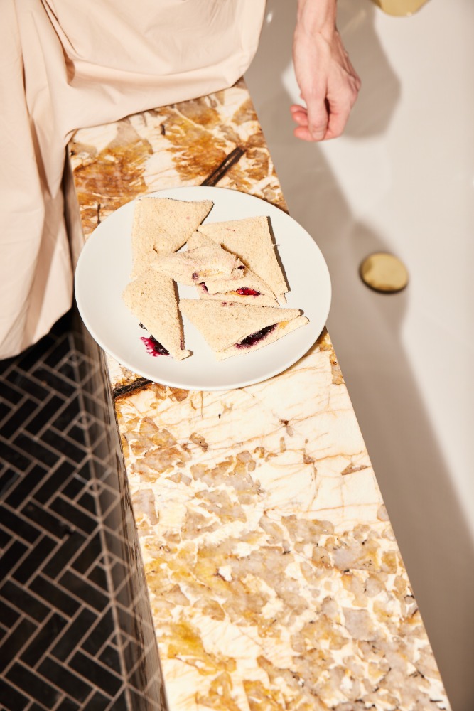 Overhead shot of triangular sandwiches with visible filling on a white plate, placed on a marble surface near a bathtub.