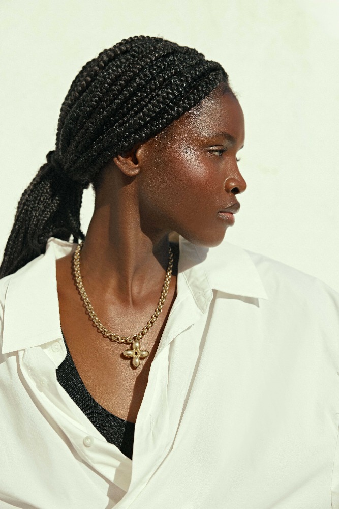Close-up portrait of an adult woman with braided hair wearing a white collared shirt and a gold pendant necklace in a photo studio.