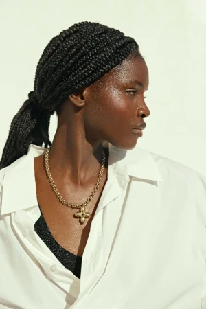 Close-up portrait of an adult woman with braided hair wearing a white collared shirt and a gold pendant necklace in a photo studio.