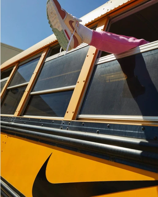 View of a pink-clad leg and white sneaker emerging from a school bus window, contrasting with the bus's yellow and black exterior.