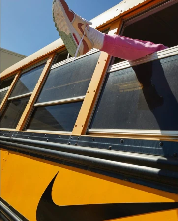 View of a pink-clad leg and white sneaker emerging from a school bus window, contrasting with the bus's yellow and black exterior.