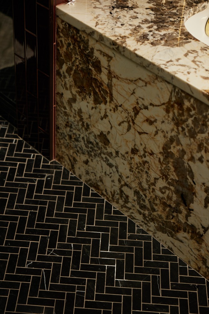 Close-up of a bathroom with black herringbone tile flooring and a stone countertop with dark brown veining, creating a luxurious aesthetic.