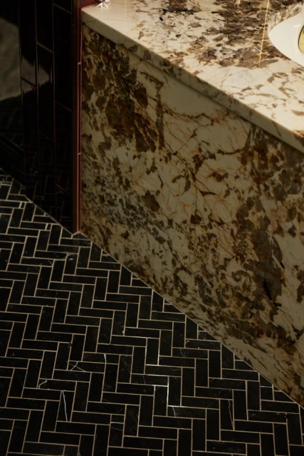 Close-up of a bathroom with black herringbone tile flooring and a stone countertop with dark brown veining, creating a luxurious aesthetic.