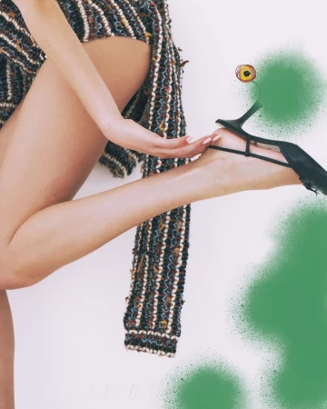 Striking fashion shot showcasing a woman's legs, a textured coat, and a black high heel with artistic green spray paint accents.