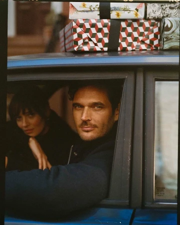 Handsome man in a blue car with a woman, packages on the roof, medium shot, portrait orientation, outdoor setting, lifestyle, fashion editorial.