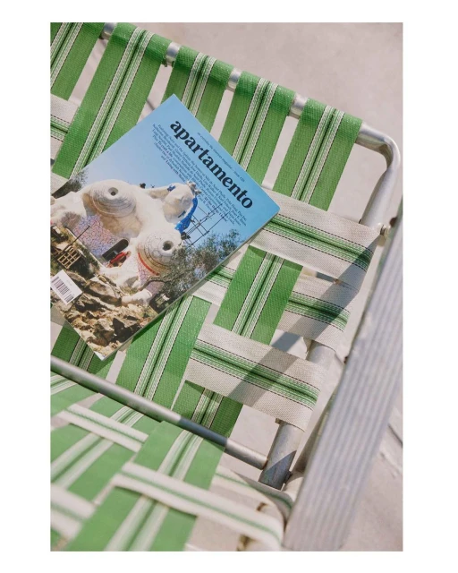 Magazine titled 'apartamento' displayed on a green and white striped lawn chair outdoors, catching sunlight, creating a serene visual.