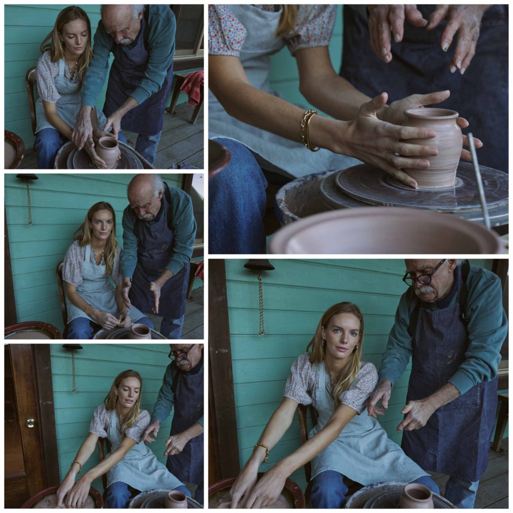 An elderly man teaching a younger woman pottery. The pair are indoors, shaping a clay pot on a pottery wheel. They both wear aprons.