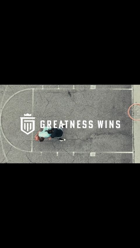 High-angle aerial view of two people playing basketball on an outdoor asphalt court with white court lines.