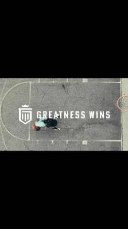 High-angle aerial view of two people playing basketball on an outdoor asphalt court with white court lines.
