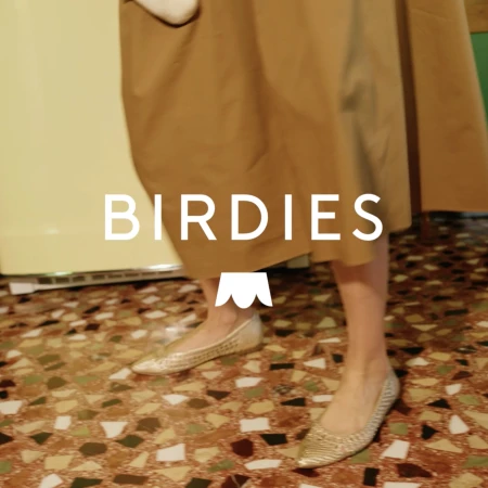 Person wearing metallic gold flats standing on a speckled tile floor next to a beige refrigerator